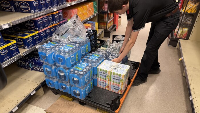 Un employé d'un magasin se penche pour prendre un sac de bouteilles d'eau.   