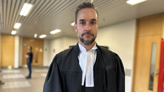 Un avocat en toge regarde l'objectif avec un air sérieux.