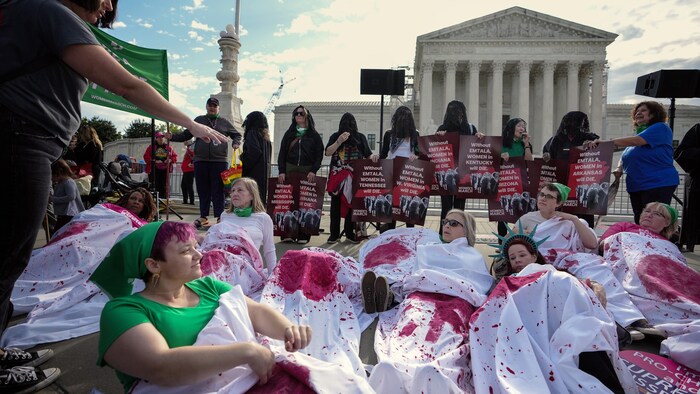 Des femmes manifestent pour le droit à l'avortement devant la Cour suprême des États-Unis. Certaines sont couchées au sol, sous des draps blancs tachés de sang. 