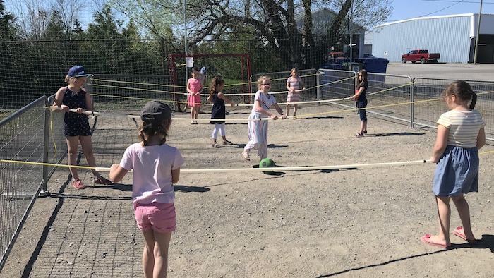 Des enfants sur un terrain tiennent des cordes et se passent un ballon.