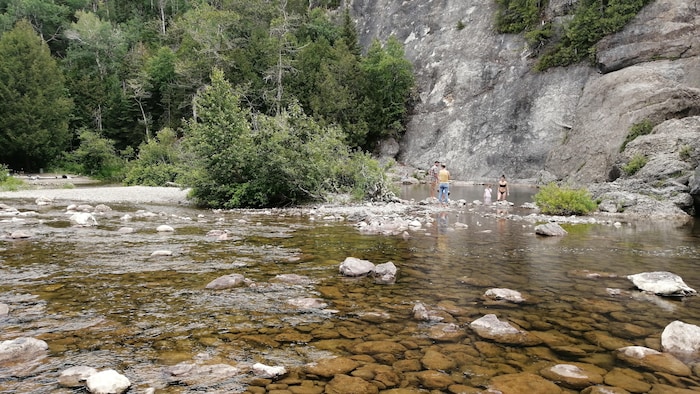 Les pieds dans l'eau, deux couples se trouvent au pied d'une paroi rocheuse.