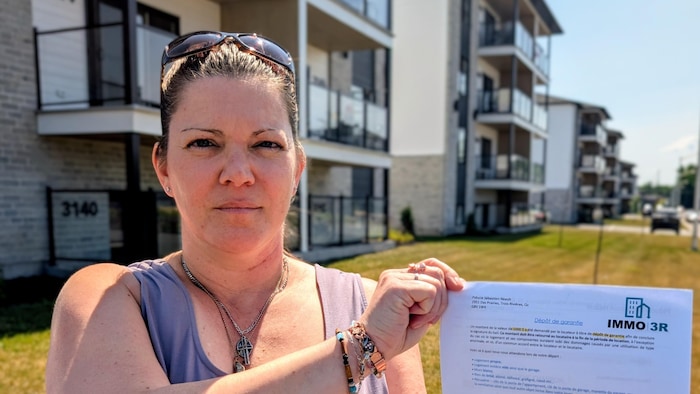 Une femme devant un immeuble à logements montre son bail.