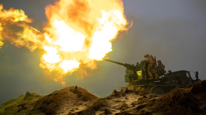 Une boule de feu sort du canon d'un char sur lequel se trouvent deux soldats.