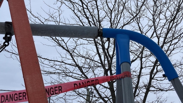 Une banderole « danger » est accroché sur le poteau d'une balançoire.