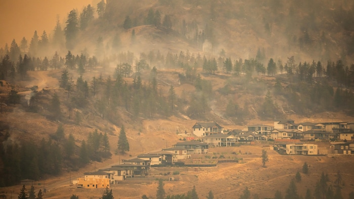 Habitations situées sur un flanc de montagne enfumé et orangé.