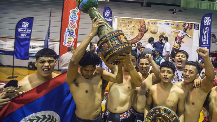 Des joueurs de balle maya du Belize, torse nu, soulèvent le trophée des vainqueurs.