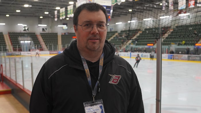 Un homme pose pour la photo devant une patinoire où des personnes jouent.