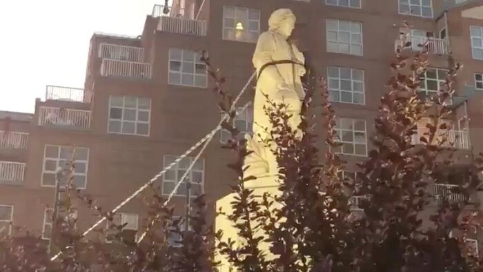 Une statue de Christophe Colomb devant un immeuble est entourée d'un câble pour la faire tomber.