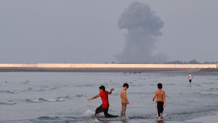 Des enfants s'amusent dans l'eau avec une fumée d'explosion en arrière-plan.