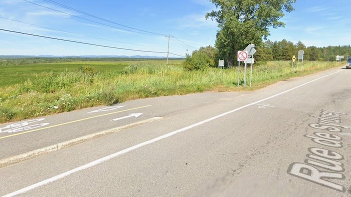 Une piste cyclable balisée longe une route rurale près d'un panneau d'interdiction aux bicyclettes.