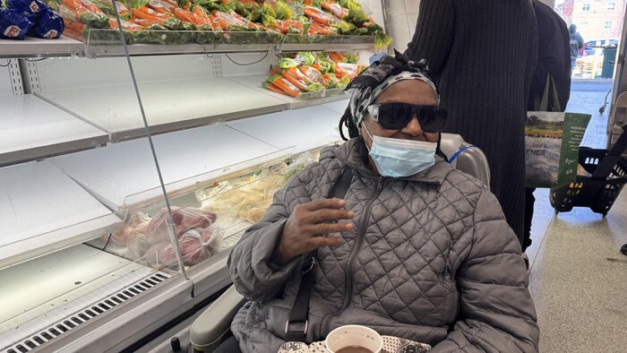Gloria, assise dans son fauteuil motorisé, devant les étagères de la banque alimentaire.