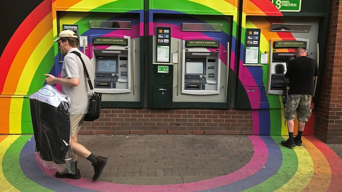 Un client retire de l'argent à un distributeur automatique de la banque Toronto-Dominion (TD), décoré aux couleurs du drapeau arc-en-ciel de la Fierté.