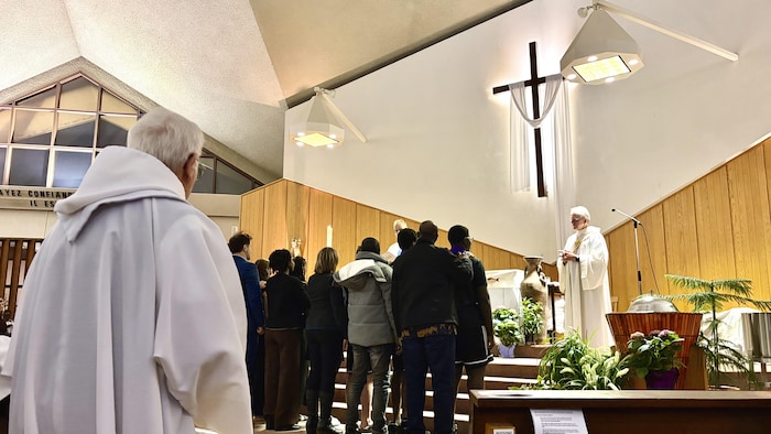 Un prêtre regarde un groupe de personnes rassemblé au bas des marches du chœur d'une église. 