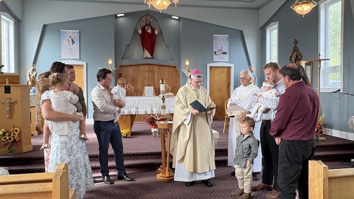 Un prêtre tient une bible entouré de paroissiens avec des enfants, lors d'un baptême.