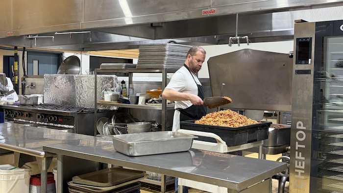 Un cuisinier en train de faire des pâtes bolognaise, dans une grande cuisine.