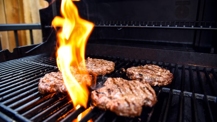 Des hamburgers grillent sur un barbecue avec de grandes flammes.