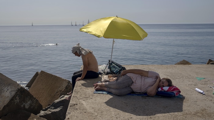 Bir kadın, İspanya'nın Barselona kentinde sahilde bir şemsiyenin altında uyuyor. 