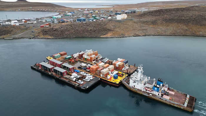 Un navire transportant trois barges se dirige vers une communauté.