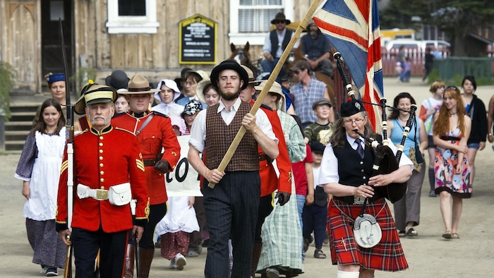 People dressed in traditional 19th century clothing lead a tourist parade down a street in Barkerville.