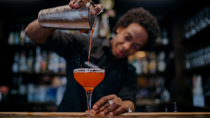 Un barman verse un cocktail dans un verre.
