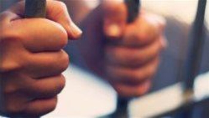 Deux mains tiennent des barreaux de prison. 