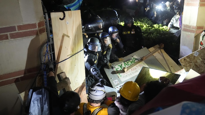 Des policiers et des manifestants se font face dans un enchevêtrement de panneaux de contreplaqué.