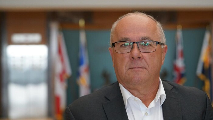 Debout dans un corridor bien éclairé, Barry Petten regarde droit devant lui et affiche un air très sérieux.