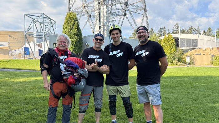 Quatre hommes souriants au pied de la tour de la Cité de l'énergie.