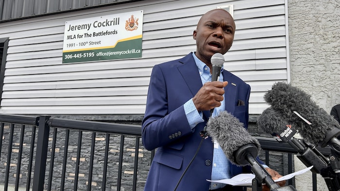Bashir Jalloh parle à un micro devant les bureaux de Jeremy Cockrill.