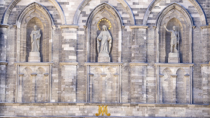 Trois statues sur un fond de pierres grises.