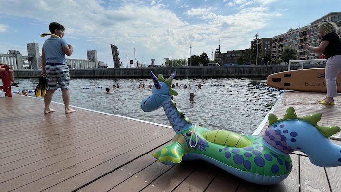 Des gens se baignent dans la bassin Louise alors qu'un enfant les regarde, sur le bord du quai.