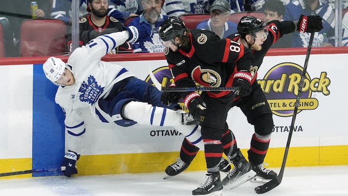 Le joueur d'Ottawa Adam Gaudette (81) fait tomber Steven Lorentz (18) samedi 26 avril 2025, le long des glissières de la patinoire.