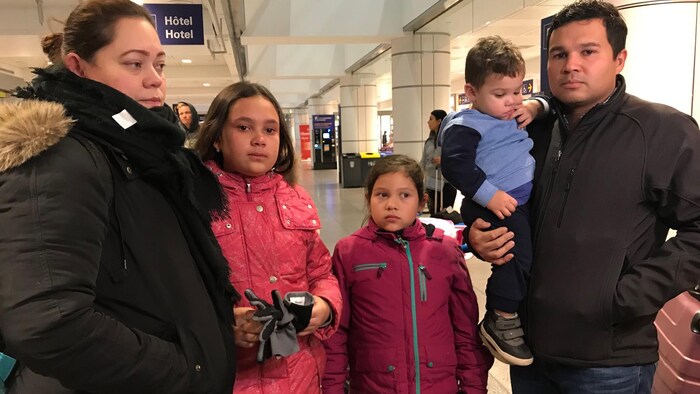 La famille, composée des parents et de trois enfants, le regard triste, attend de prendre l'avion à l'aéroport.