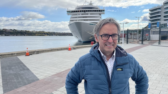 René Trépanier, directeur général de l'Association des croisières du Saint-Laurent, sourit à la caméra sur un quai de Québec devant un bateau de croisières.