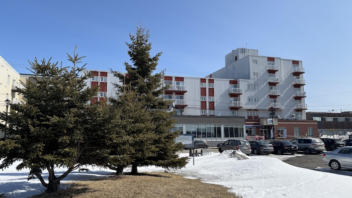 Un bâtiment de tôle photographié en hiver. Des résineux en cachent une partie.