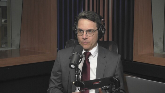 Un homme est assis derrière un micro de Radio-Canada dans un studio de radio.