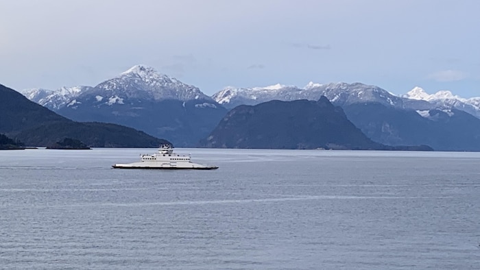 Un traversier de BC Ferries sur la baie Howe avec des montagnes enneigées en arrière-plan.