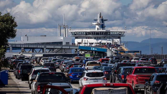 File d'automobiles devant un traversier sur fond de soleil et de nuages.