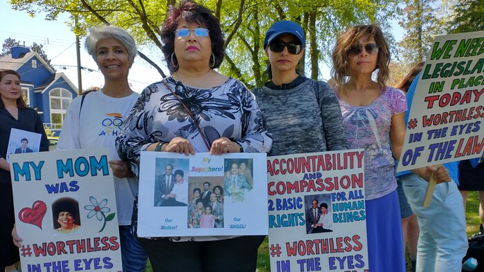 Quatre femmes tiennent des pancartes à la mémoire de leur proche, Theresa Pereira, pour réclamer un changement à la loi nommée Family Compensation Act, en Colombie-Britannique.