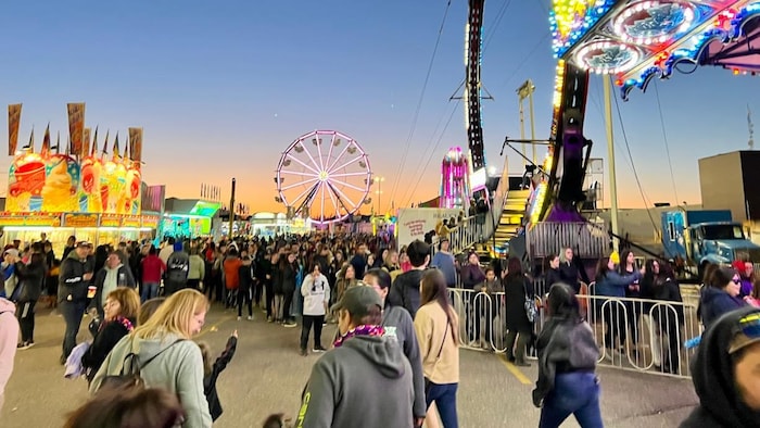 Entre les manèges et les kiosques de nourriture, une foule dense se promène à la foire.