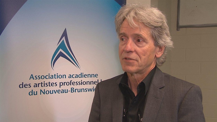 Philippe Beaulieu en entrevue devant une affiche de l'Association