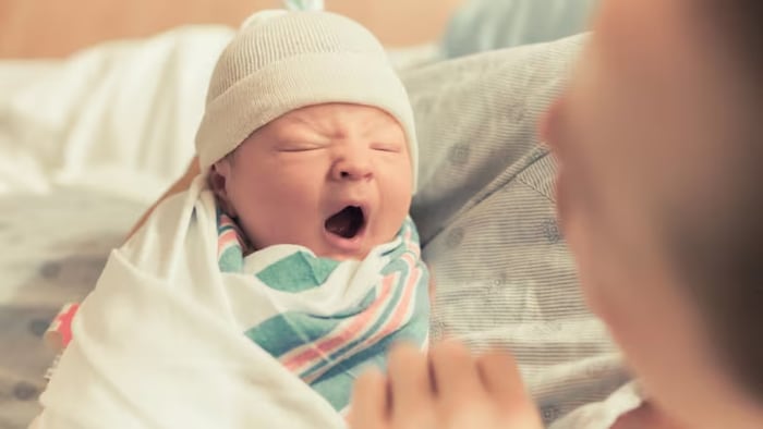 Un bébé baille dans les bras d'une femme.