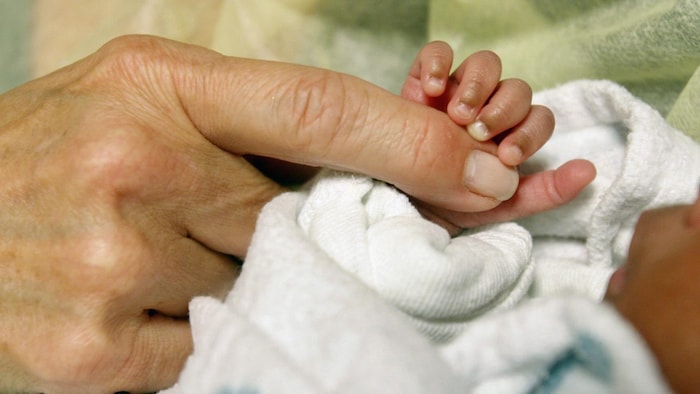 Gros plan des doigts d'un bébé serrant l'index d'une femme.