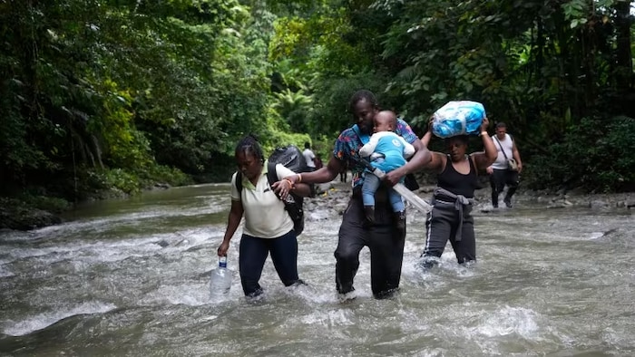 Haitian migrants wade through a river as they cross the Darien Gap, from Colombia into Panama, hoping to reach the U.S. on Oct. 15, 2022. One expert says the number of migrants making the perilous crossing suggests this summer will break all previous records for irregular migration into North America. (Fernando Vergara/Associated Press)