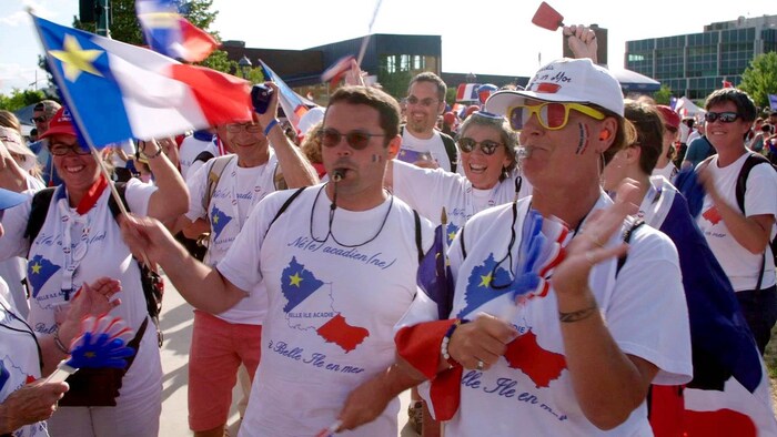 Des Bellilois, sifflets à la bouche, portant des chandails de l'Acadie et agitant des drapeaux de l'Acadie.