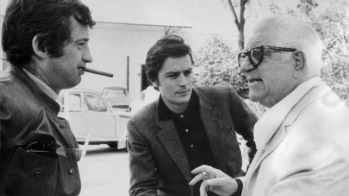 Les trois hommes discutent ensemble. Jean-Paul Belmondo fume une cigarette.