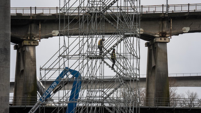 Deux ouvriers sont sur des échafaudages accrochés au pont Pattullo.