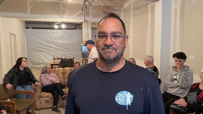 Un homme portant des lunettes et un t-shirt bleu marine posé en premier plan.