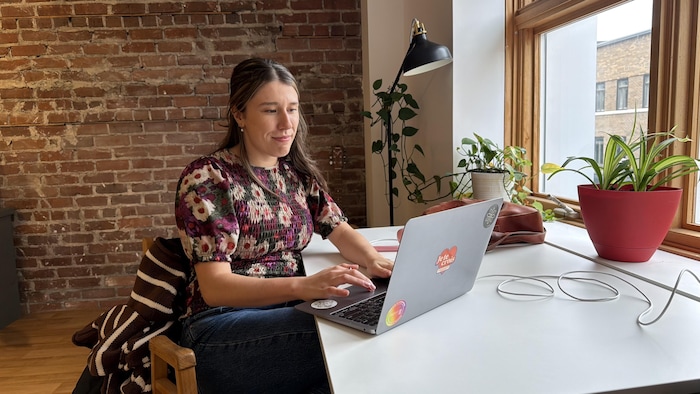 Une femme assise à un bureau blanc travaille sur un ordinateur portable.