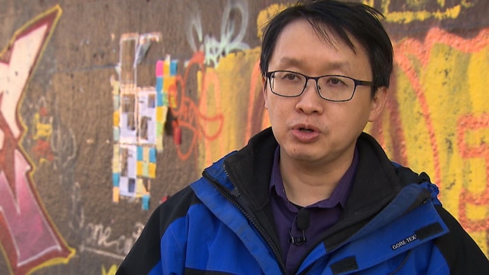 Benjamin Fung en entrevue devant un mur sur lequel se trouvent des graffitis.